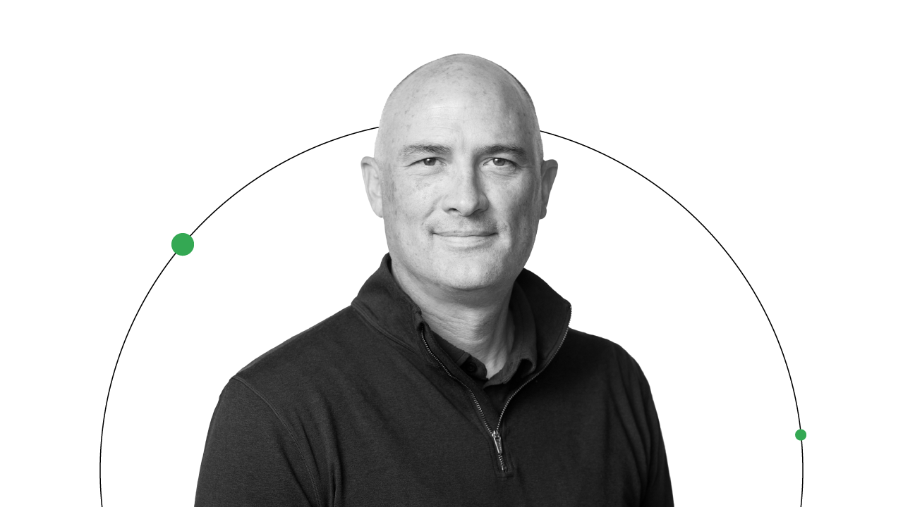 Brendon Kraham, VP of search and commerce global ads solutions at Google, is pictured from the shoulders up, smiling. Kraham has light skin and eyes, and wears a dark zip-front pullover. A thin black line with a two greens dot frames his portrait.