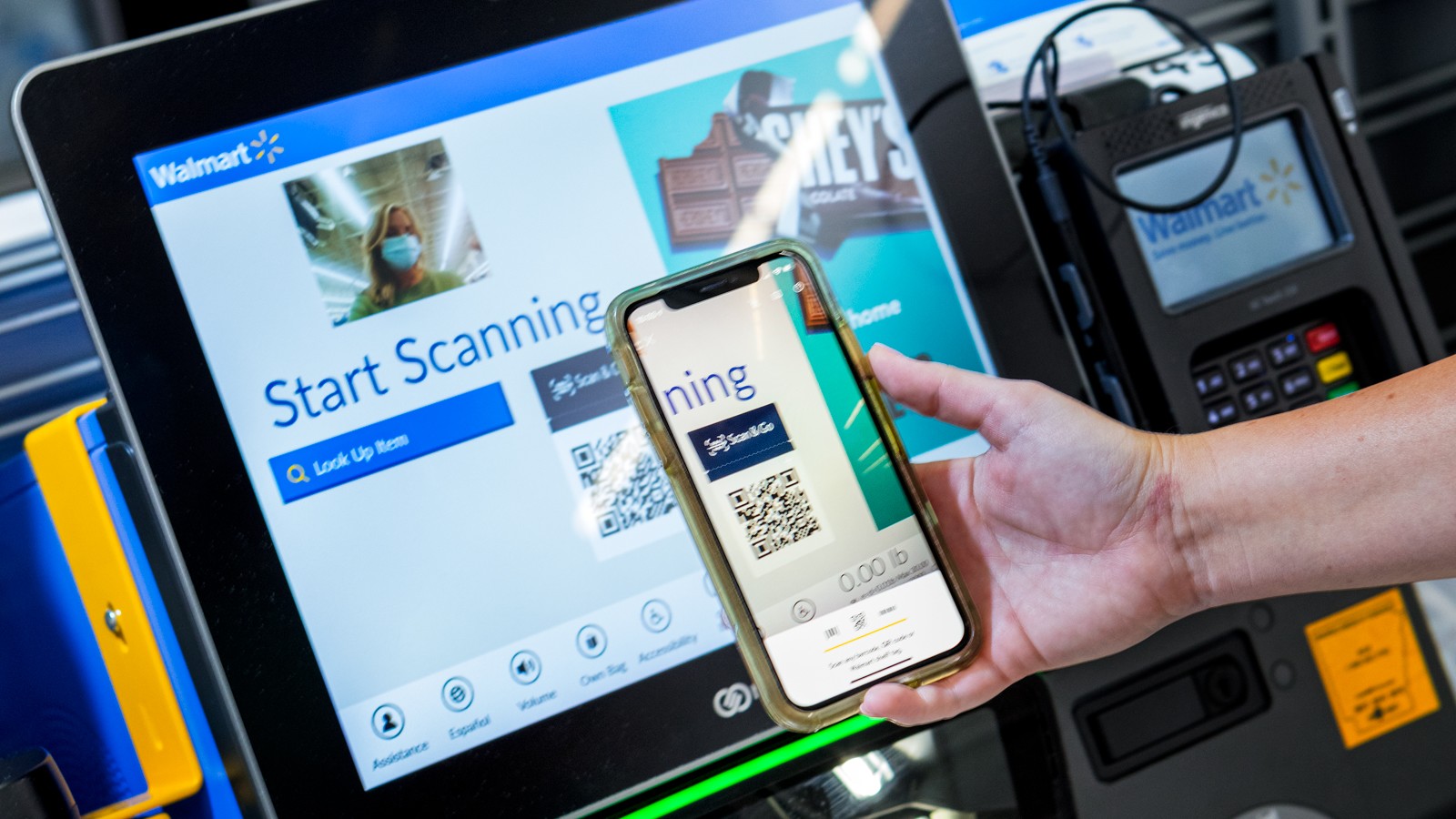 A shopper uses their smartphone camera to scan a QR code displayed on a Walmart self-checkout screen.