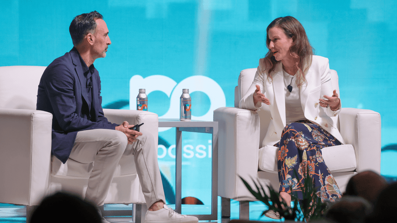 Sean Downey, président d'Americas & Global Partners chez Google, est assis à côté de Laura Jones, CMO d'Instacart, sur la scène de la conférence "Possible Miami", devant un arrière-plan bleu vert, décoré d'un paysage urbain et de palmiers.